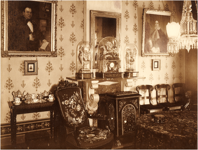 180948 Woonkamer in het huis van de familie Coovels-Bots met aan de muur schilderijen met links Gerardus J. Coovels en ...