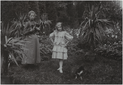 181045 Louisa Petronella Michaella Henrica Maria Coovels (Louise) met links een vrouw met twee hondjes in de tuin van ...