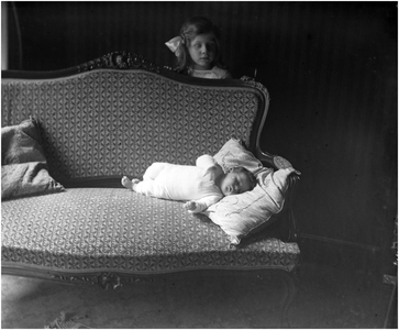 182145 Paul van Thiel ligt op de sofa terwijl Louise van Thiel over de sofa heen toekijkt, 02-07-1916