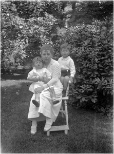 182227 Louise Coovels met Paultje en Yvonne van Thiel samen op een stoel in de tuin, z.j.