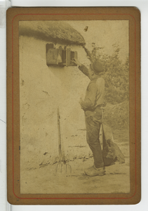 390092 Man bij een vogelkooi aan een gevel van vitselwerk, ca. 1890