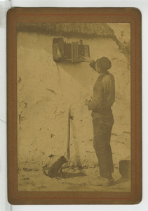 390093 Man bij een vogelkooi aan een gevel van vitselwerk, ca. 1890