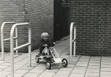 195780 Kind op een skelter fietsend tussen de hekjes geplaatst op het trottoir om voetgangers te beschermen tegen ...