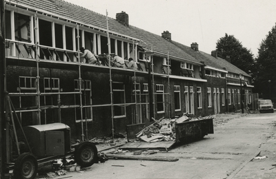 195969 Het werken aan woningen door bouwvakkers op stijgers tijdens de renovatie, op de voorgrond een container met ...