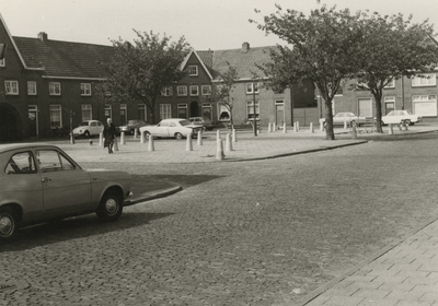 196024 Straat niet bekend; geparkeerde auto's rond een plein, dame met boodschappentas, 1979