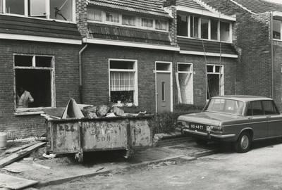 196035 Het werken van een bouwvakker aan een van de huizen, voor de deur een container met puin, 1977