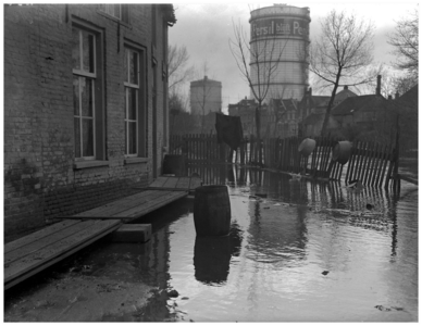 128284 Overstroming van de Dommel in de omgeving van de Plekhoek. Op de achtergrond de gashouders en de huizen aan de ...