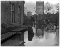 128284 Overstroming van de Dommel in de omgeving van de Plekhoek. Op de achtergrond de gashouders en de huizen aan de ...