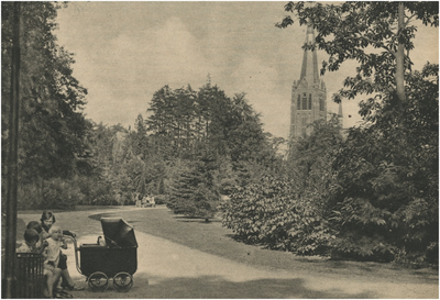 193881 Vrouw en kinderen zitten op een bankje in het Stadswandelpark. Op de achtergrond de St. Joriskerk, 1936