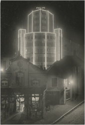 194128 Avondopname van Café Central/ Tramhalt van C. v.d. Hogen - v.d. Hurk, met daarachter de Lichttoren van Philips ...