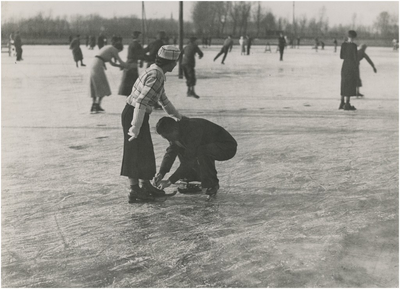 195108 Schaatsen: het recreatief schaatsen, sportpark, Aalsterweg. Man en vrouw, het strikken van een schaatsschoen, 12-1935