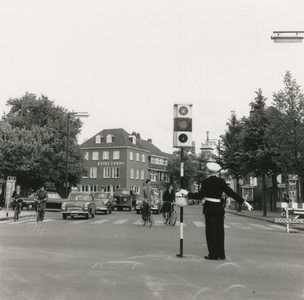 195744 Auto's en fietsers, politeman met stoplicht, op het midden van een kruispunt, regelt het verkeer, 1961-1965