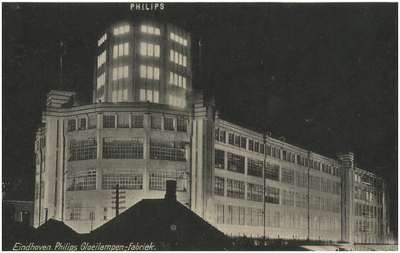 220738 Avondopname van de Philips lichttoren, Mathildelaan, met op de voorgrond enkele woningen en winkels, 1935 - 1940