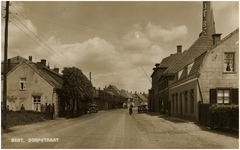 12715 Hoofdstraat, vanaf spoorweg gezien richting kerk, met rechts de schoorsteen van weverij TRICOT BEST, waarachter ...