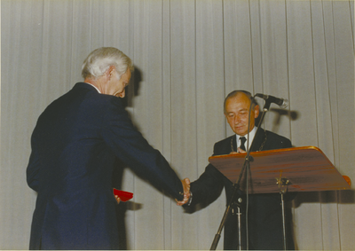 135030 Burgermeester Bonnier reikt aan een der onderscheidende van de fanfare de koninklijke onderscheiding uit, 16-10-1987