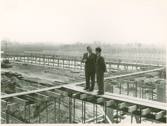 135100 Weth Braam met de aannemer boven op de steiger bij het in aanbouw zijnde nieuwe beton fabriek te Son, 26-04-1956