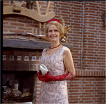 254904 Vrouw van de fotograaf poseert voor een openhaard, op de schouw een geweer, 04-1960