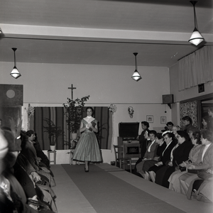 255025 Mannequin showt toeschouwers een jurk op de catwalk, 1955