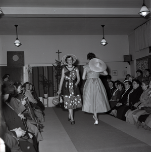 255027 Twee mannequins showen de toeschouwers hun jurk en zonnehoed op de catwalk, 1955