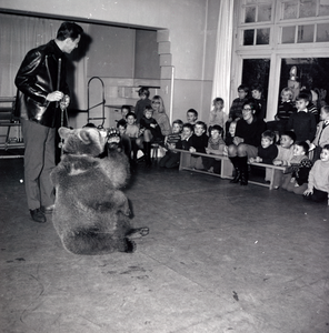 255037 Kleuters en juf kijken naar de dierentemmer met een zittende beer , 1965