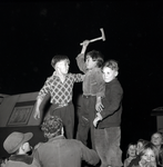 255093 Jongens op toneel, een met een hakbijl. toeschouwers, 12-1955