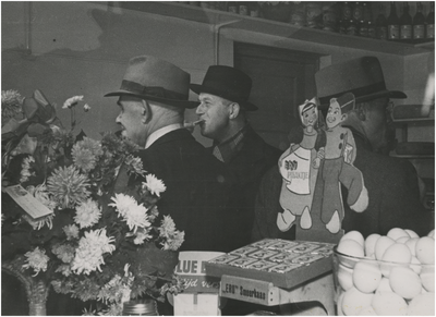196489 In het midden de burgemeester en rechts wethouder Janssens in een zuivelwinkel, 08-11-1947