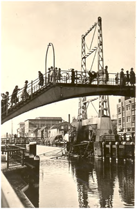 109847 De voetgangersbrug over het kanaal. Daarachter de opgeblazen Veestraatbrug. Rechts de beschadigde panden aan de ...