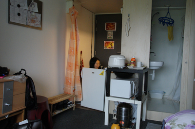 505537 Kamer in woonblok, TU terrein: Caixia Liu zit achter de koelkastdeur.in de kamer een badkamer, friteuse, ...