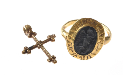  Foto van het gouden kruisje en ring. De ring heeft een fantasie schrift rondom een (hergebruikte) gem. In de gem is ...