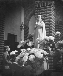 276161 Seminaristen plaatsen bloemen bij het beeld van de H. Gabriël in de kerk van klooster St. Gabriel te Haastrecht