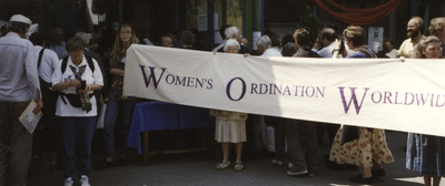 152134 Zuster Annemarie Stijnman houdt een spandoek vast (boven de letter O) met de tekst 'Women's Ordination Worldwide'