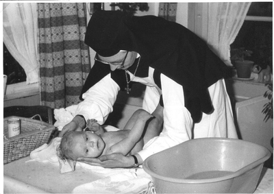 152361 Zuster Aniceta verschoont een baby in de bewaarschool te Rozenburg