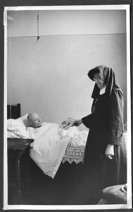 258008 Zuster Mariëtte bezorgt de krant bij een patiënt op bed in het pension te Kloosterburen