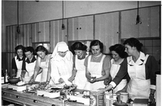 258018 Zuster Adelheid in de keukenvaardigheidsklas van de HHS (huishoudschool) in Tilburg
