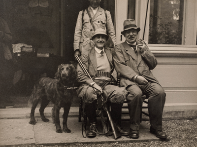  Drie jagers, waarvan twee zittend, met hond voor de veranda van huis Wickenburgh te 't Goy