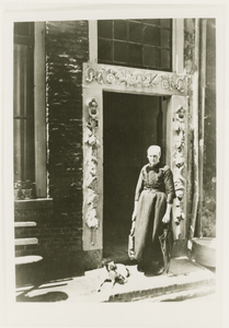 1142 - Weduwe Jentje Bosman staande bij een deur met antieke omlijsting van hardsteen,   voorstellende symbool van ...