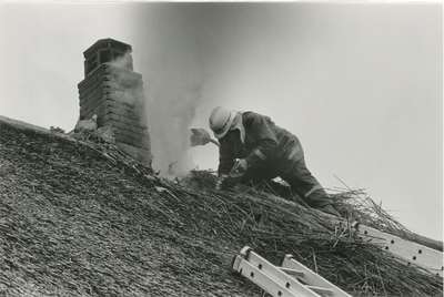 4589 - Brandweerman bezig met een schoorsteenbrand op een rieten dak.