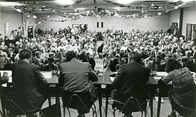 9381 - Veiling Hotel Ittmann; zaal met mensen op rijen stoelen; op voorgrond mensen achter tafels; aan