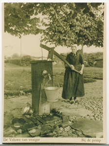 14662 - Een boerin in, zo het lijkt, Puttense klederdracht, pompt water uit de pomp op een boerenerf