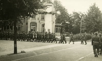 16864 - Een groep militairen marcheert voorbij een villa in Jugendstil naar de kazerne