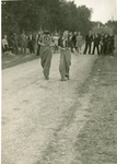 16895 - Bevrijdingsfeest Tonsel. Twee vrouwen doen een wedstrijd zaklopen. Zeventien buurtgenoten kijken toe