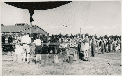 16942 - Een luchtballon wordt aan de grond gehouden door zandzakken en lijnen. Een scoutinggroep, de padvinderij, helpt ...