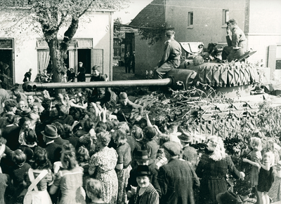 16998 - Grote groep mensen staan rondom een tank waarop twee Canadezen zitten. Linksvoor staat een verpleegster van Salem