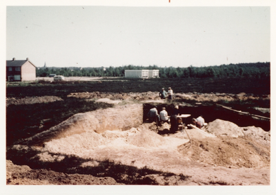 2774 - Studenten zijn bezig met archeologisch onderzoek in een grafheuvel. Op de achtergrond een houten noodschool van ...