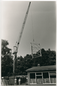 3774 - Een kraan hijst delen van een antennemast op. De mast wordt ten behoeve van de Centrale Antenne Inrichting (CAI) ...