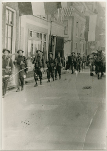 4516 - Militairen met geweer lopend door een straat; zij ogen ontspannen