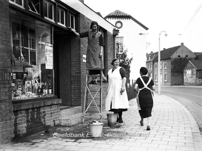 ehc_gp_116 Passerende huisvrouw groet 2 winkelvrouwen van de kruidenierswinkel, die de ramen aan het wassen zijn 29-10-1937