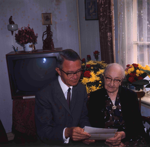 DIA_GF_1113 Een oudere vrouw (lid van de katholieke kerk) in haar huiskamer, met de pastoor; ca. 1967