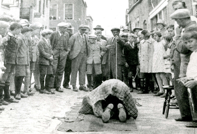 BR_KERMIS_1930_002 Vermoedelijk tijdens een kermis wordt een act opgevoerd waarbij een man geknield op een kleed op ...
