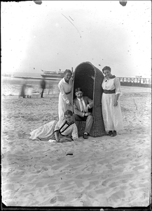 GN2243 Drie dames en een heer rond een strandstoel op het Groene Strand; ca. 1915